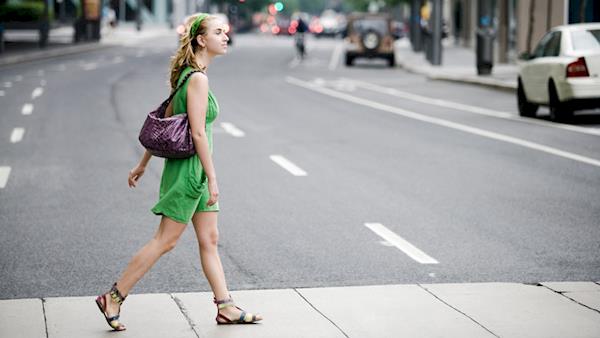 Stylishly Dressed Blonde Girl Crosses a Street in a Big City