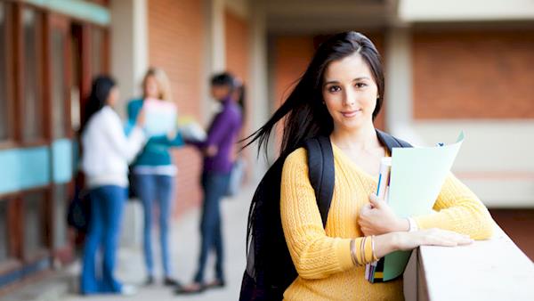 Female College Student Leaning on a Ledge Outside of a Building with other Students in the Background
